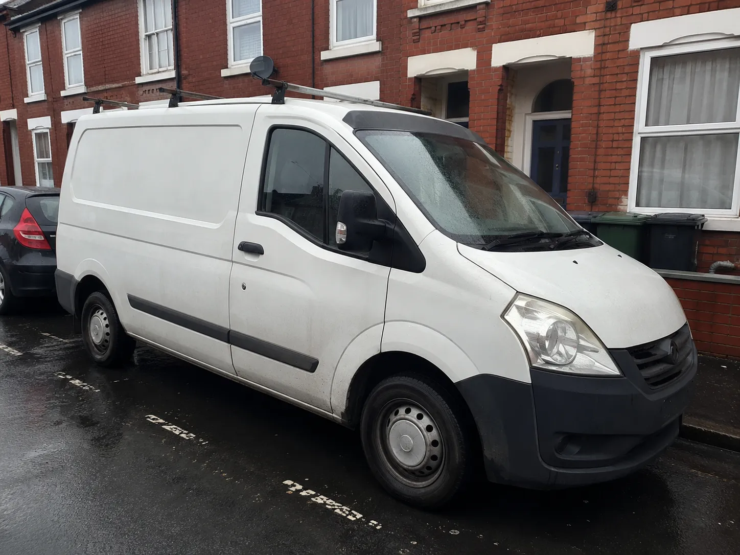A plumber's white work van parked on a red-brick terraced street in Reading on a wet day